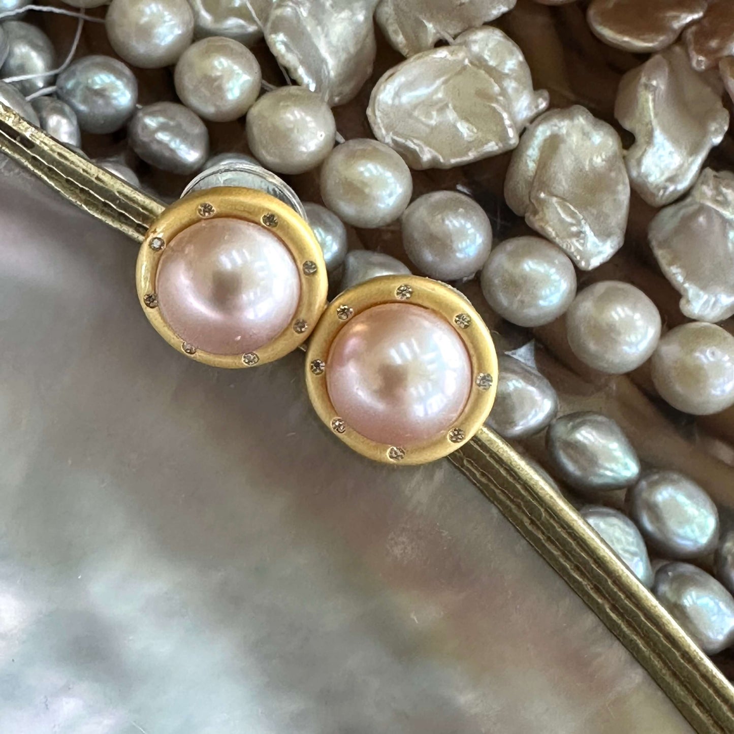Pink mabe pearl stud earrings with CZ surrounded by assorted pearls on white shell, emphasizing color contrast and luster.