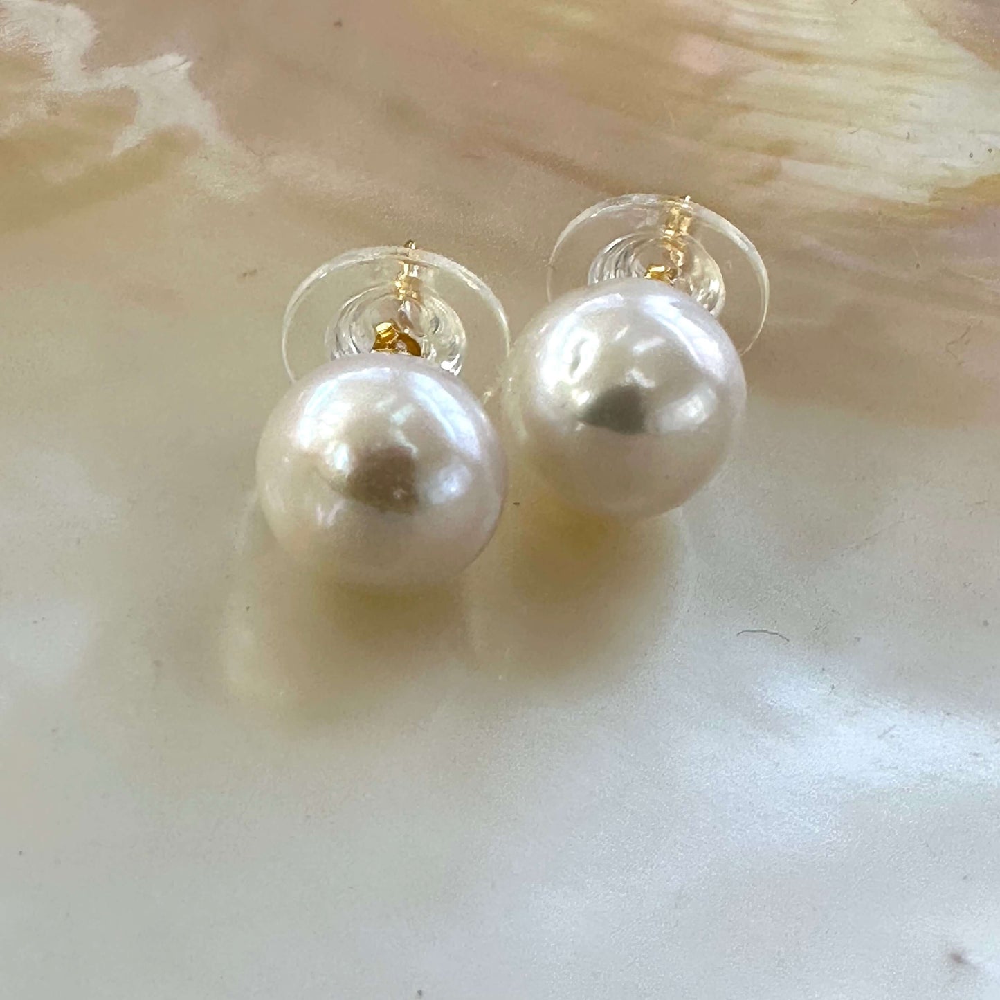 Elegant white edison pearl stud earrings displayed on white shell background, highlighting high luster and gold vermeil posts.
