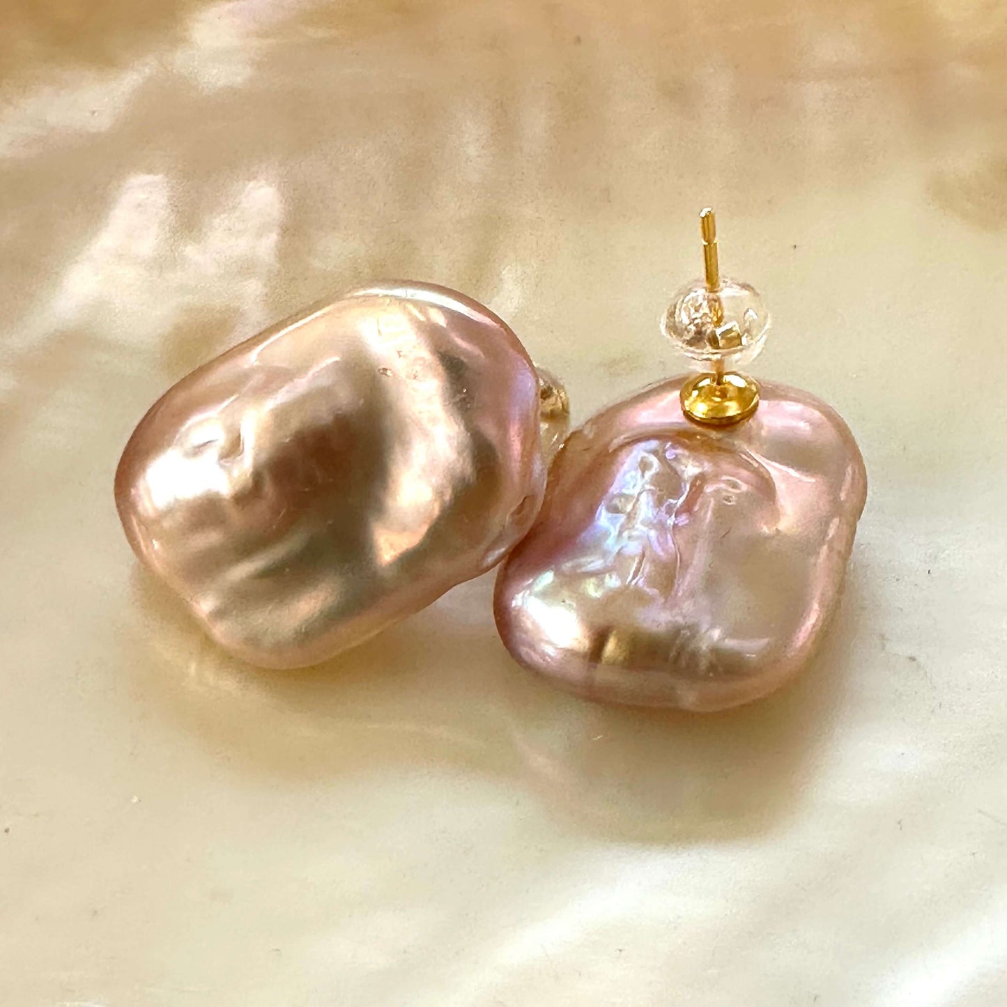 Golden pink rectangle baroque pearl stud earrings close-up on glowing yellow pearl surface, handmade in Canada.