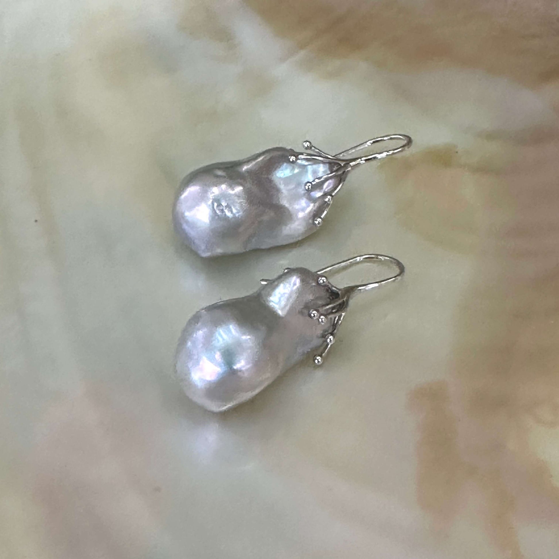 Silver grey baroque pearl drop earrings in sterling silver, close-up against white pearl shell backdrop showing lustrous surface.