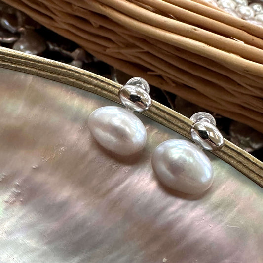 Silver grey nugget pearl stud earrings shown at an angle on pearl shell, elegant freshwater design handmade in Canada.
