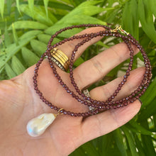 Load image into Gallery viewer, Red garnet baroque pearl necklace with a luminous Baroque pearl pendant displayed on a hand.
