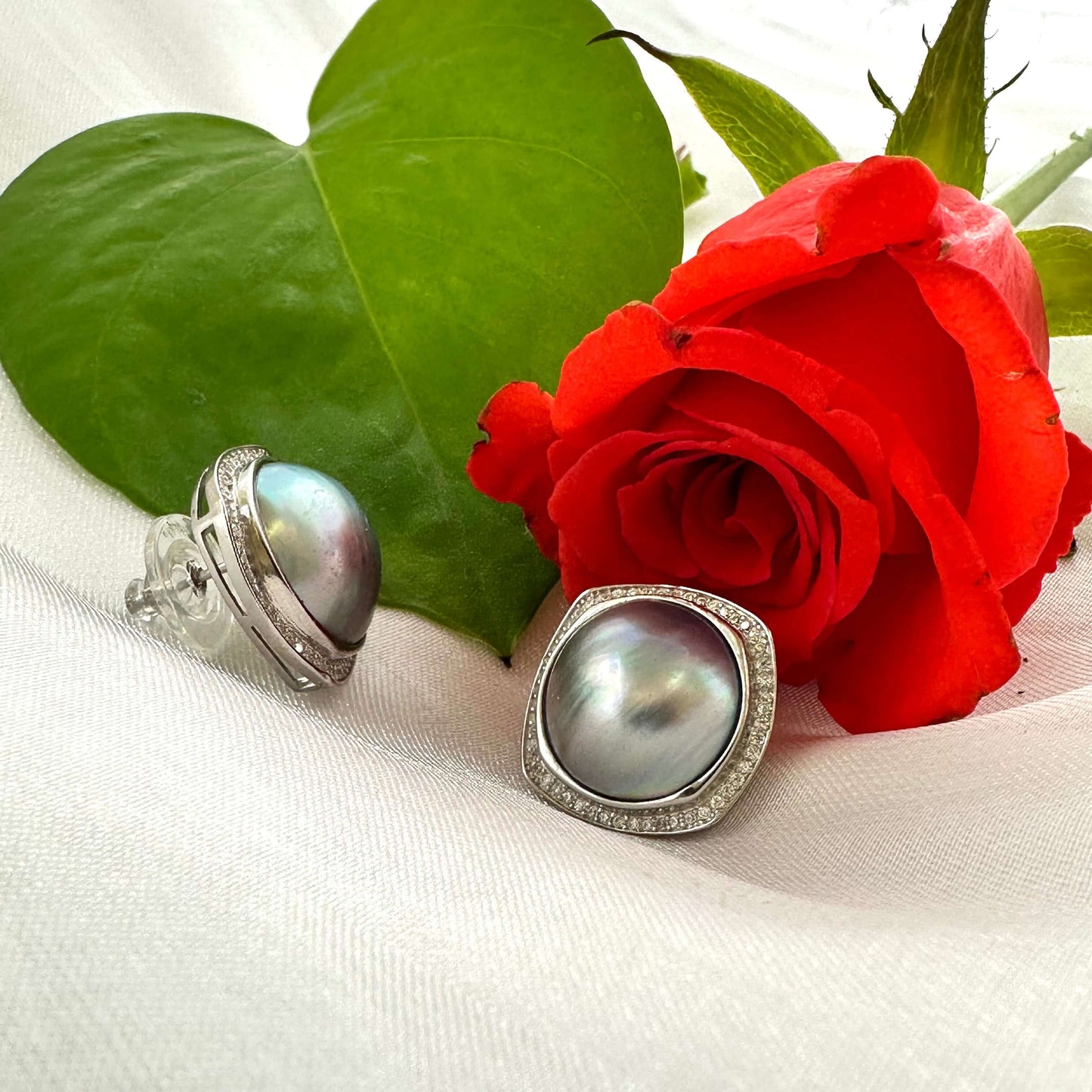 Mabe Pearl Earrings – close-up beside red rose on white fabric background