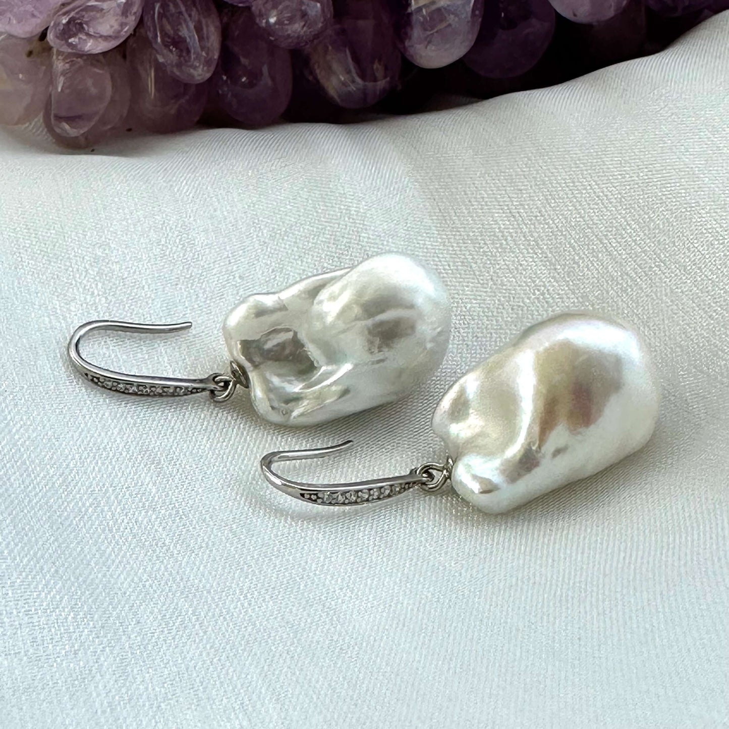 White baroque pearl bridal earrings placed on white cloth table, sterling silver CZ pavé hooks handmade in Canada.