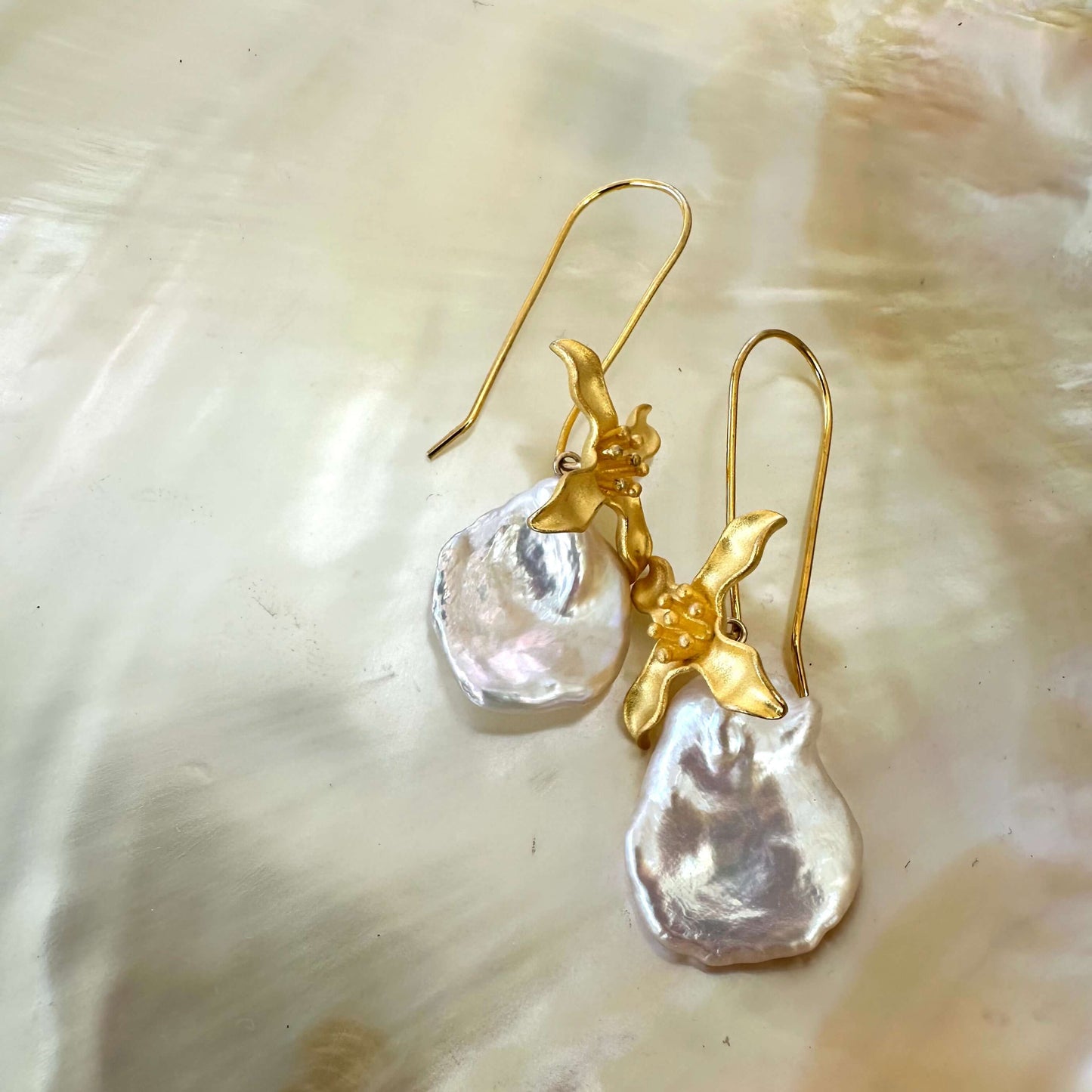 Elegant white Keshi Pearl Earrings with gold vermeil flower hooks resting on pearl shell background.