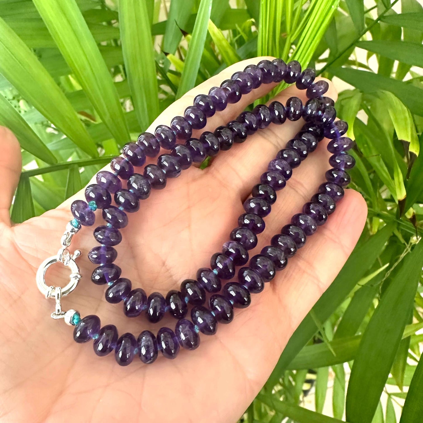 Close-up of handmade amethyst beaded necklace in dark purple tones against green leaf background