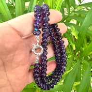 Amethyst beaded necklace held in hand for size, against green leaf background