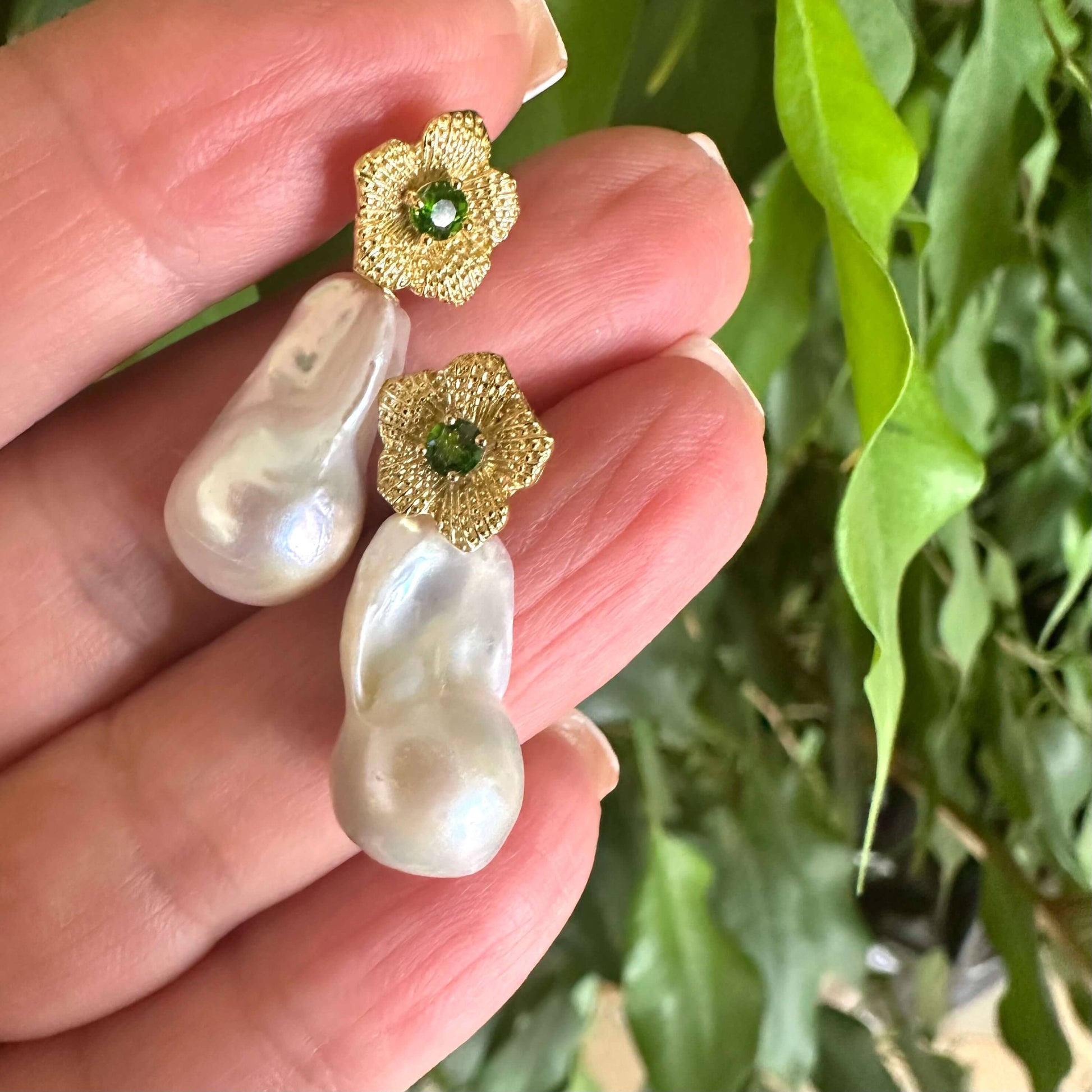 Chrome diopside pearl earrings held in hand for size comparison against green leaf background