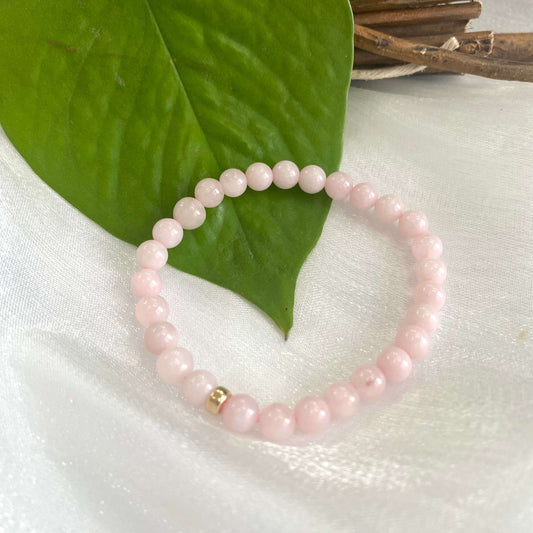 Rose quartz stretch bracelet with 6mm beads and 14K gold filled accent on a leaf background.