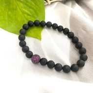 Matte black onyx mens bracelet featuring ruby red CZ spacer, stylish stretch design on a soft surface.