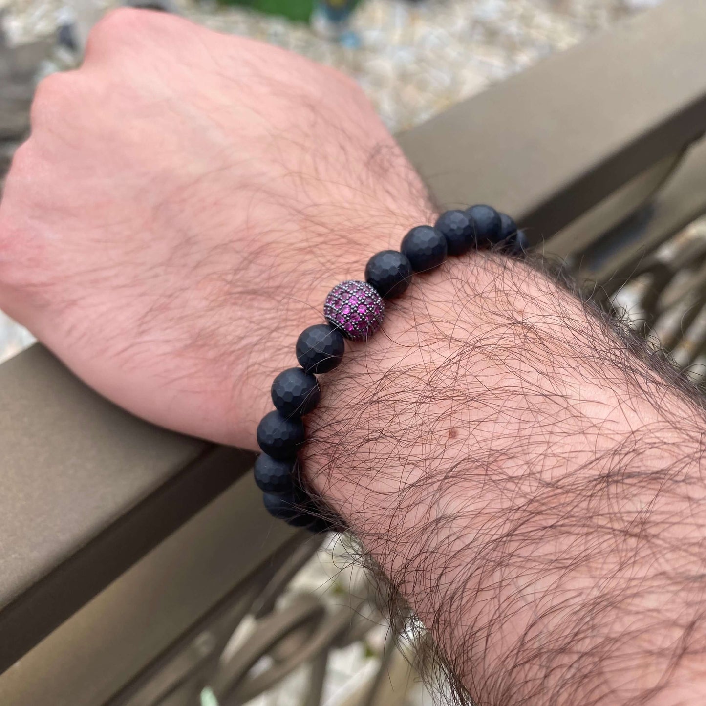 Matte black onyx mens bracelet featuring ruby red CZ, stretch design, worn on wrist.