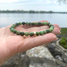 Load image into Gallery viewer, Chrysoprase stretch bracelet featuring 6mm beads with 14K Gold Filled accent, shown on hand near a lake.
