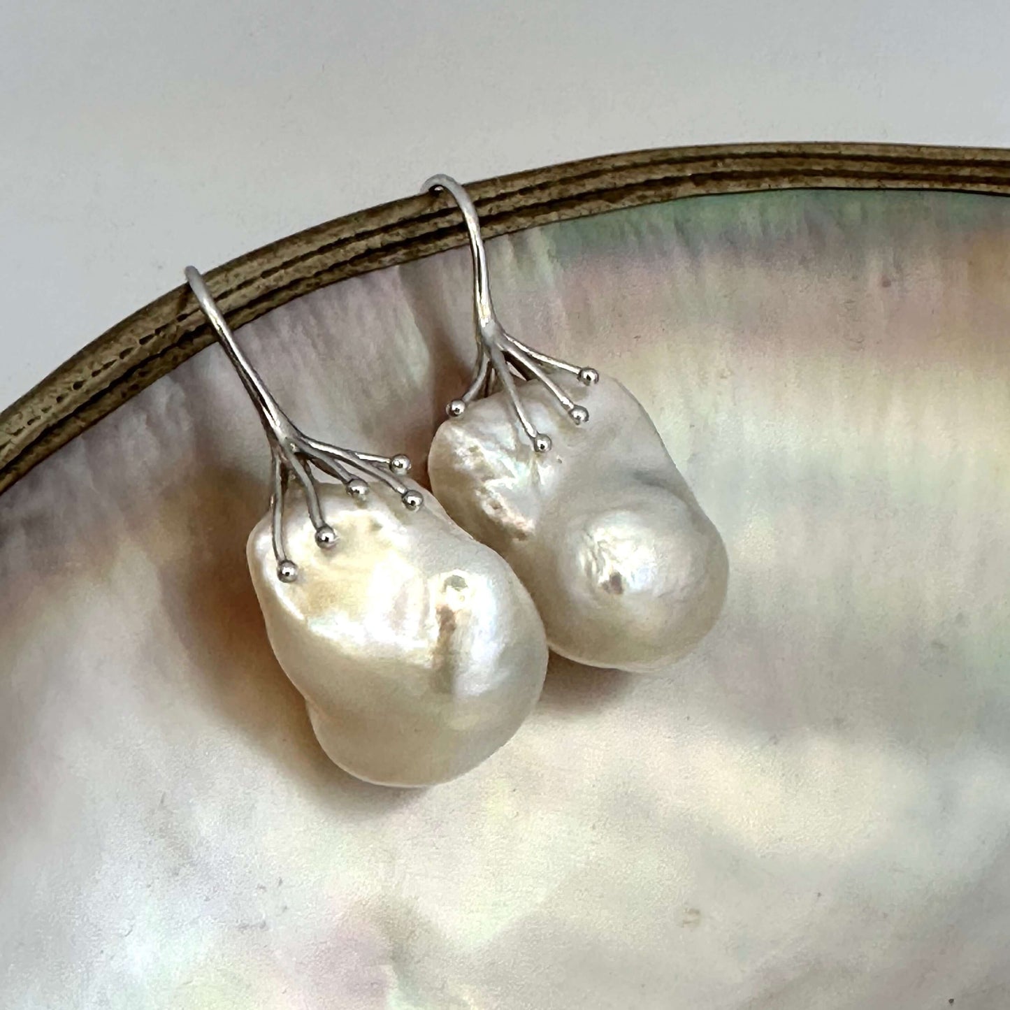 Baroque pearl drop earrings photographed on white pearl background – silver finish