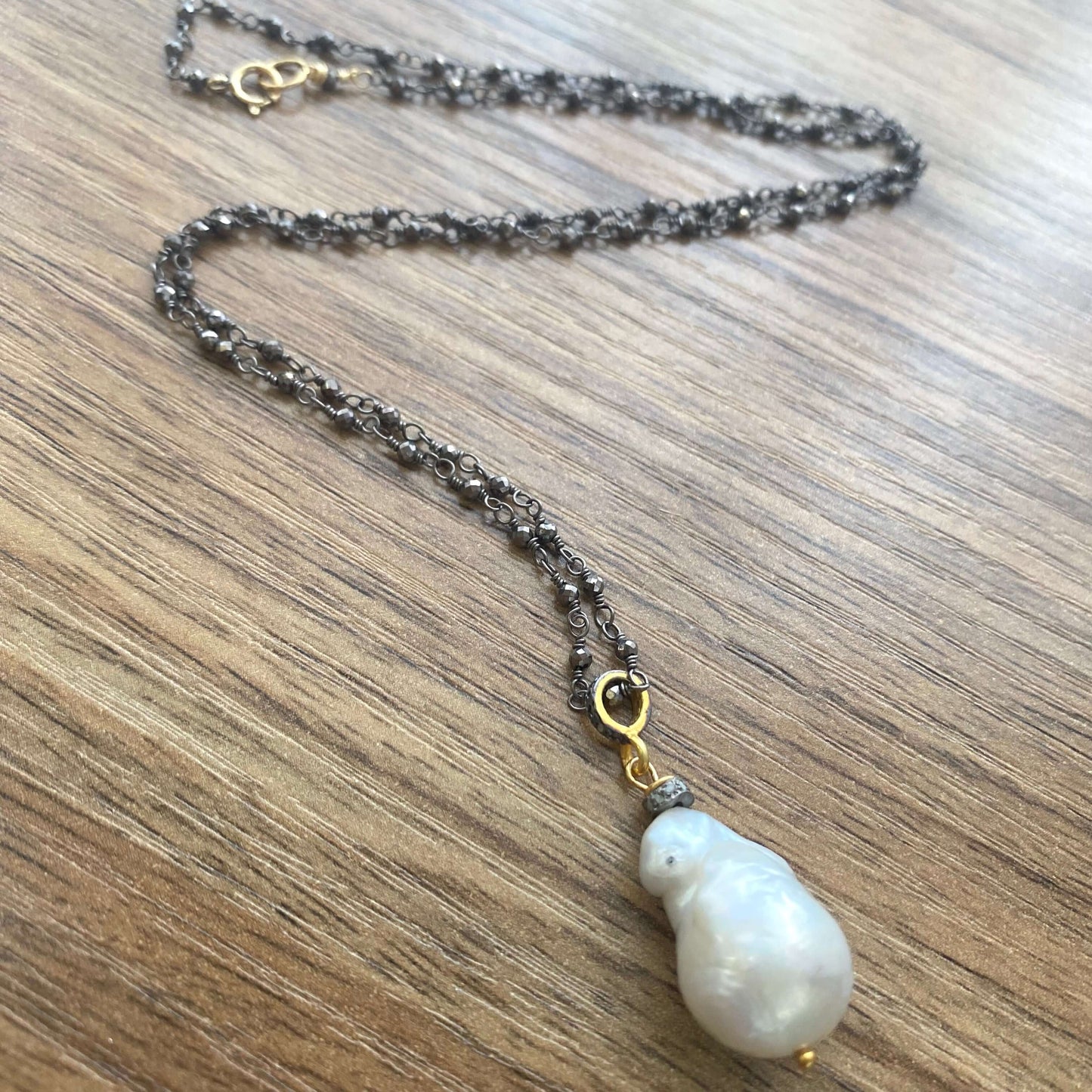 Pyrite rosary chain necklace displayed on wooden table close-up showing baroque pearl pendant