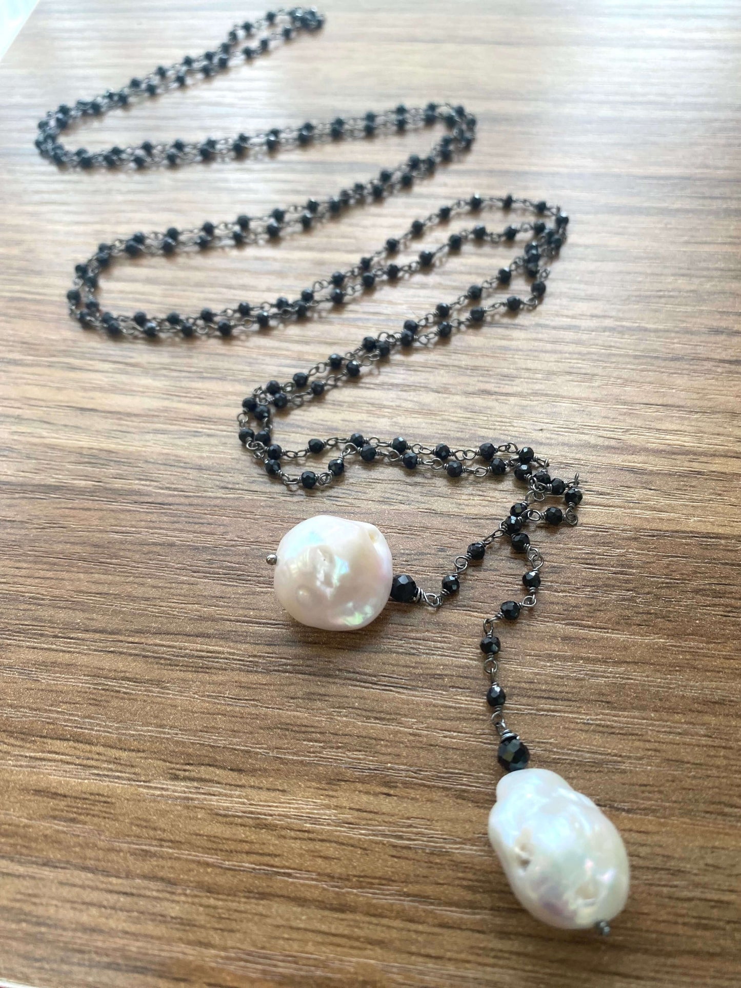 Close-up of black spinel lariat necklace on wooden table highlighting gemstones and baroque pearls