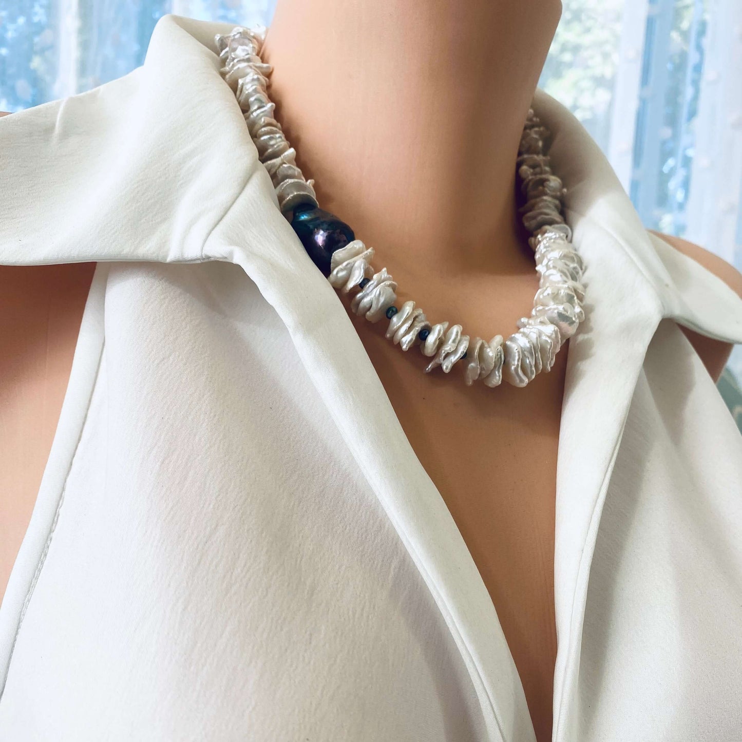 White cornflake pearl necklace with a black baroque pearl pendant elegantly draped on a mannequin.