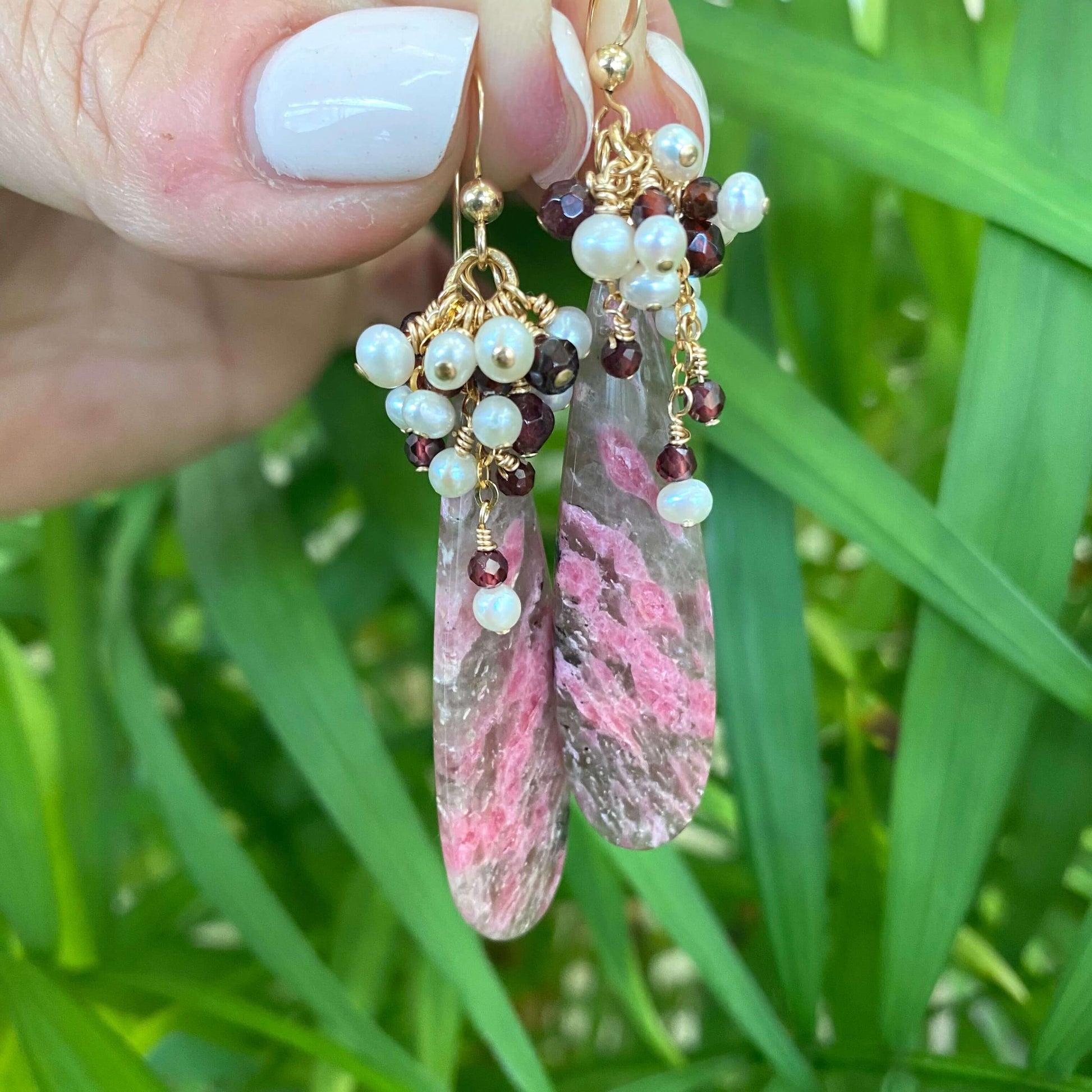 Pink rhodonite teardrop earrings close up against green foliage handmade in Canada