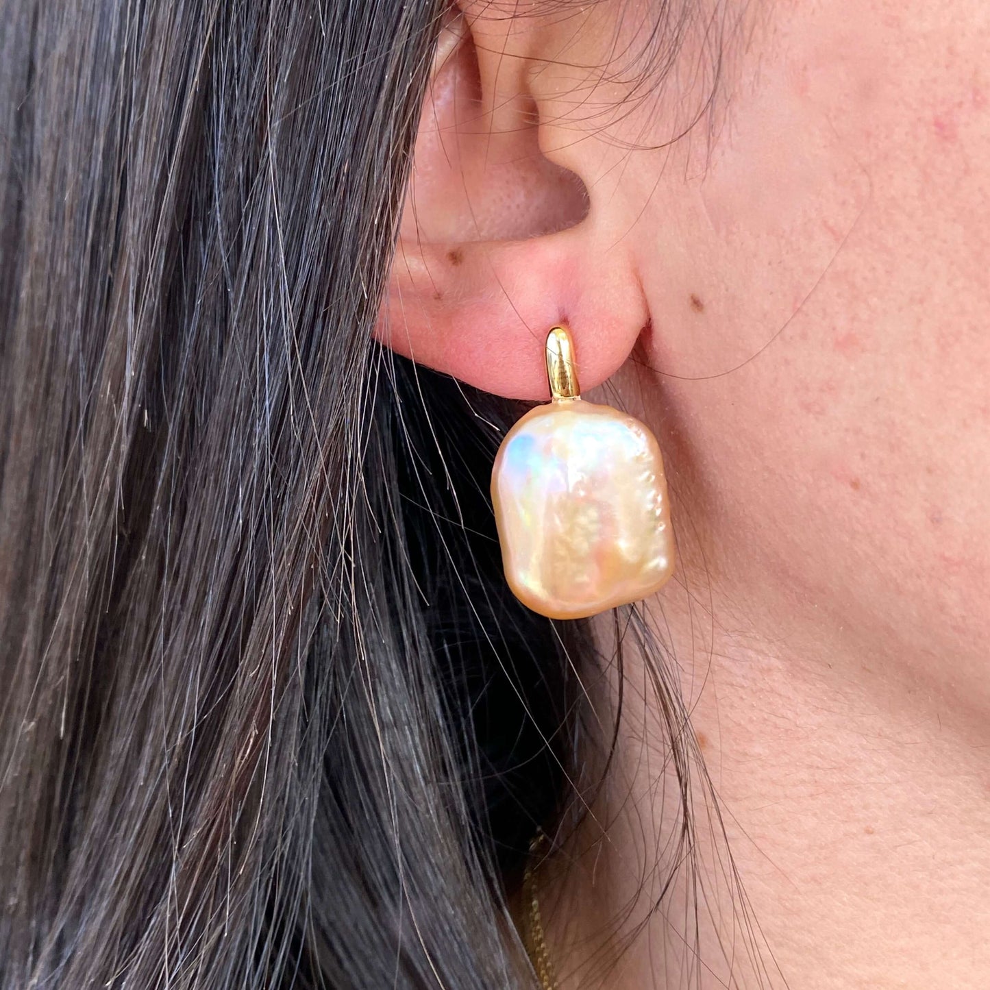 Model wearing golden peach pearl drop earrings, side profile showing rectangular baroque pearls and warm gold vermeil setting.
