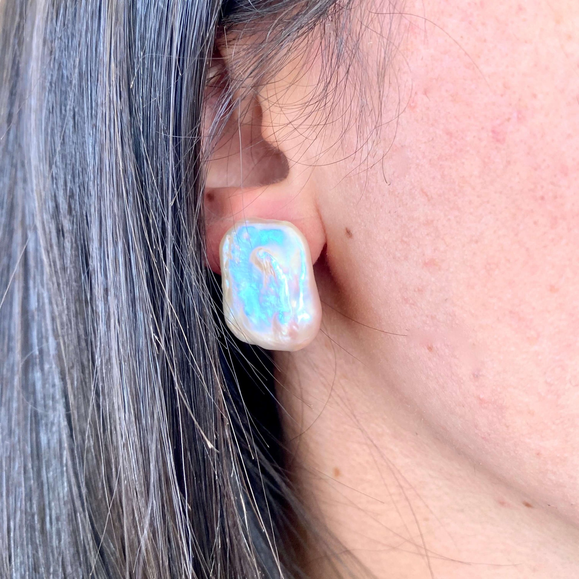 Close-up of baroque pearl stud earrings in a woman's ear showcasing their unique rectangular shape.