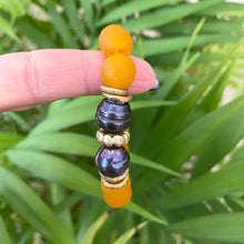 Load image into Gallery viewer, Black pearl bracelet featuring tangerine African recycled glass beads and black freshwater pearls on a finger.
