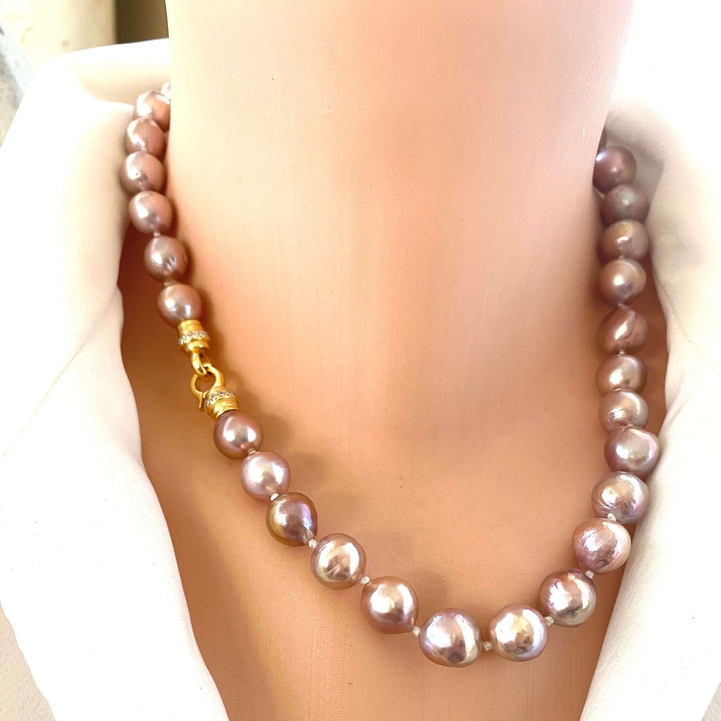 Pink lavender pearl necklace with Edison baroque pearls draped on mannequin, showing luminous surface and silver clasp.