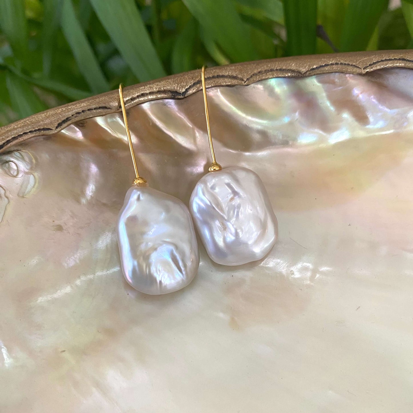 White freshwater pearl drop earrings gold vermeil version resting on shell with green foliage, handcrafted in Canada.