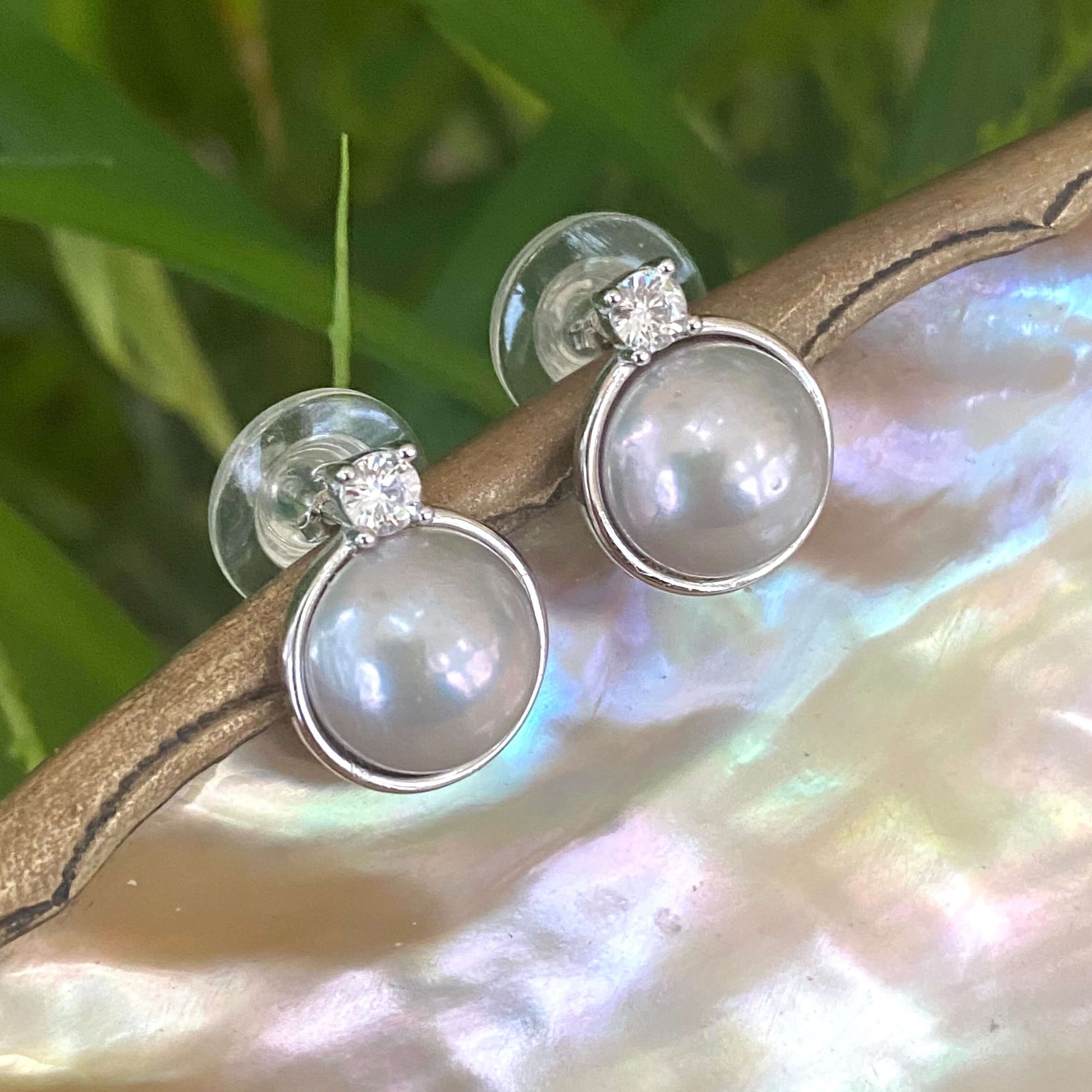 Silver grey pearl stud earrings with CZ in gold vermeil showcased on an iridescent surface.