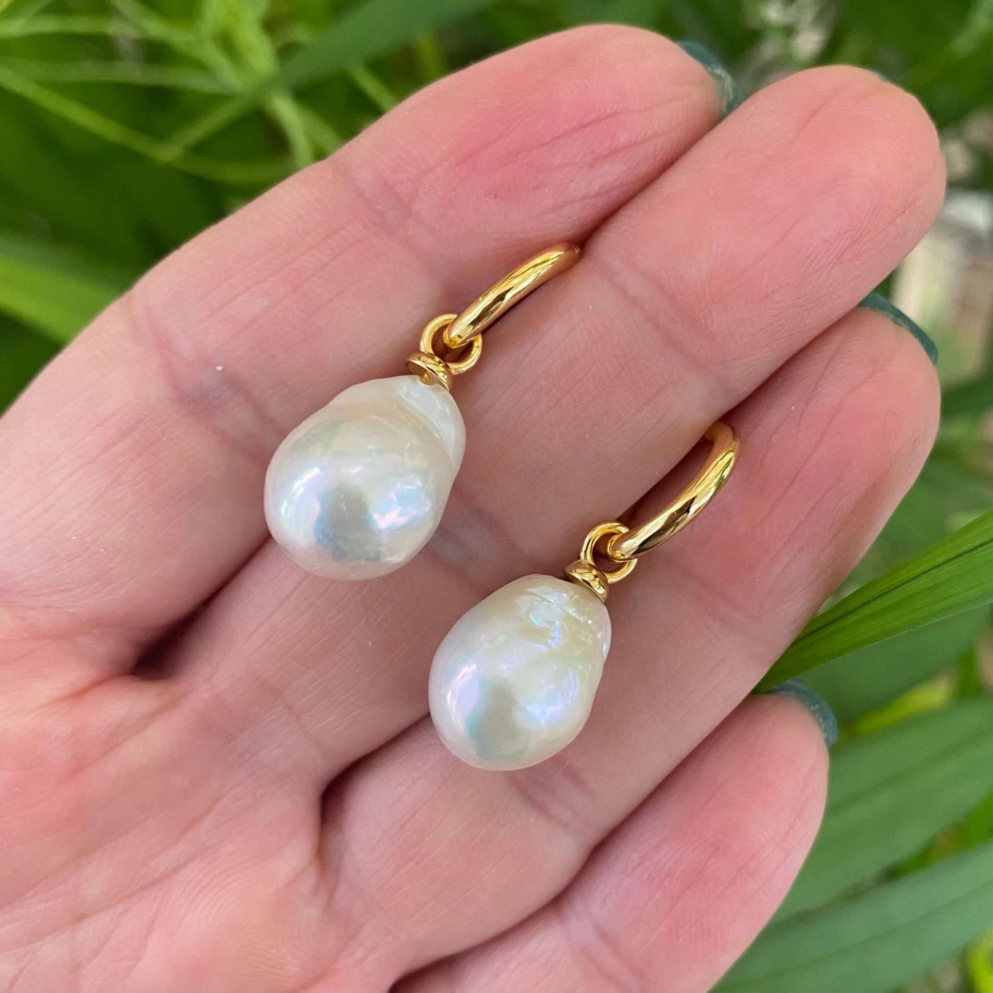 White Baroque Pearl Earrings – held by hand against natural green foliage