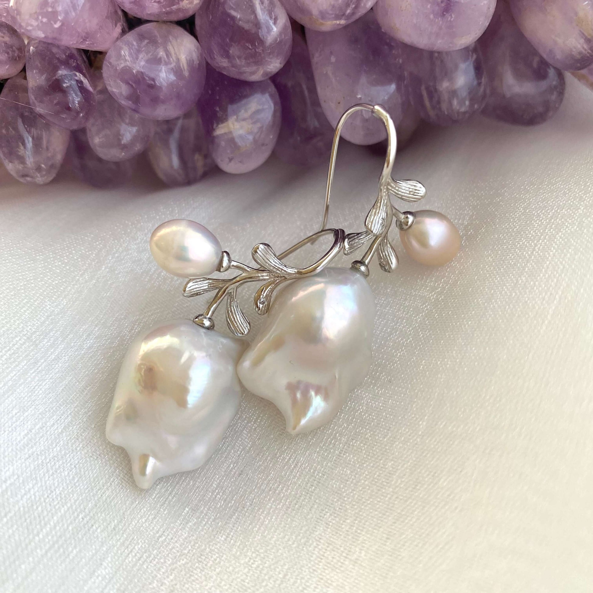 Handmade baroque pearl earrings in silver resting on white and amethyst background