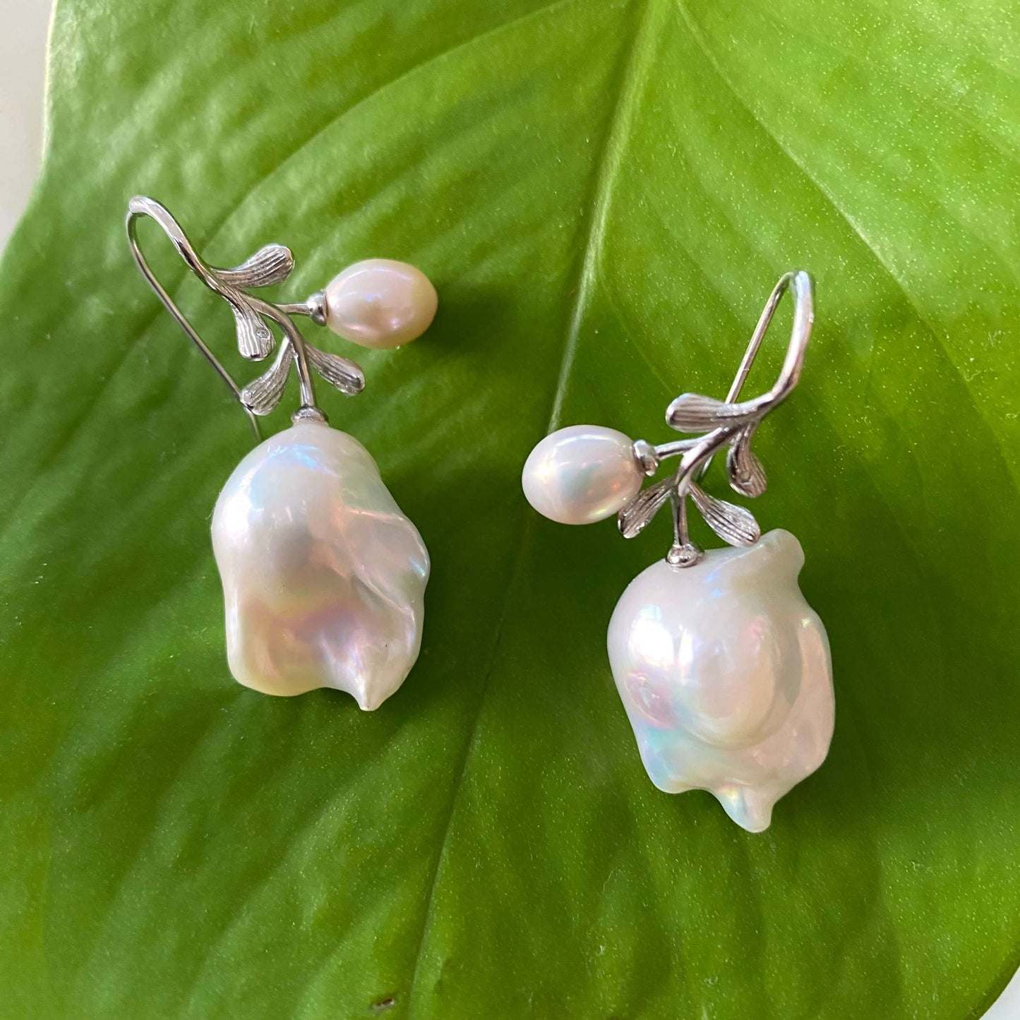 Baroque pearl earrings in silver with rose leaf design on green leaf background