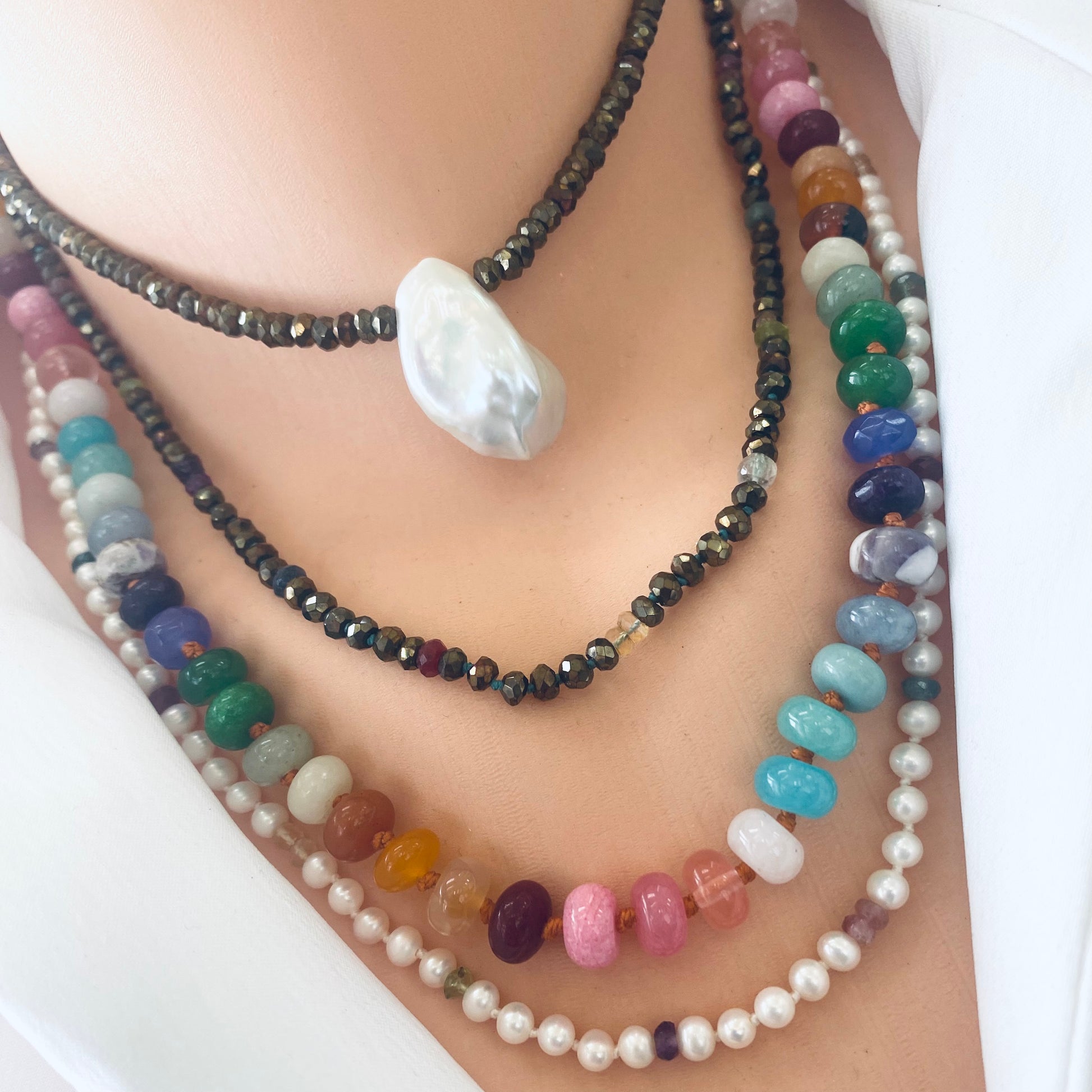 Colorful layered necklaces showcasing unique gemstone beads and a pearl pendant, emphasizing artisanal craftsmanship.