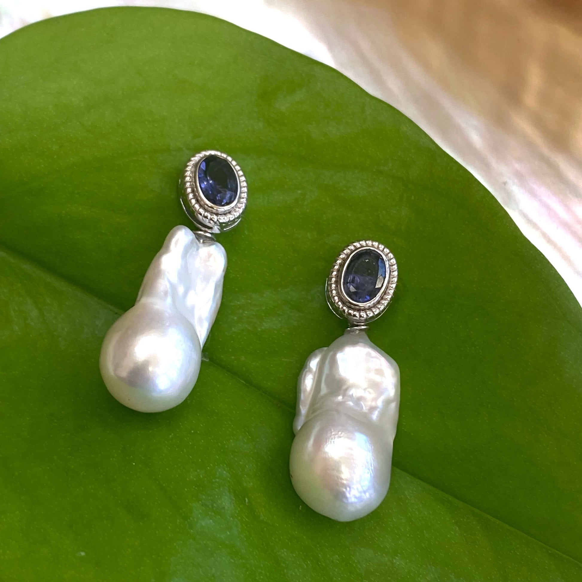 Iolite baroque pearl drop earrings photographed against green leaf background — elegant natural light jewelry shot by Loulia Pearl Jewelry