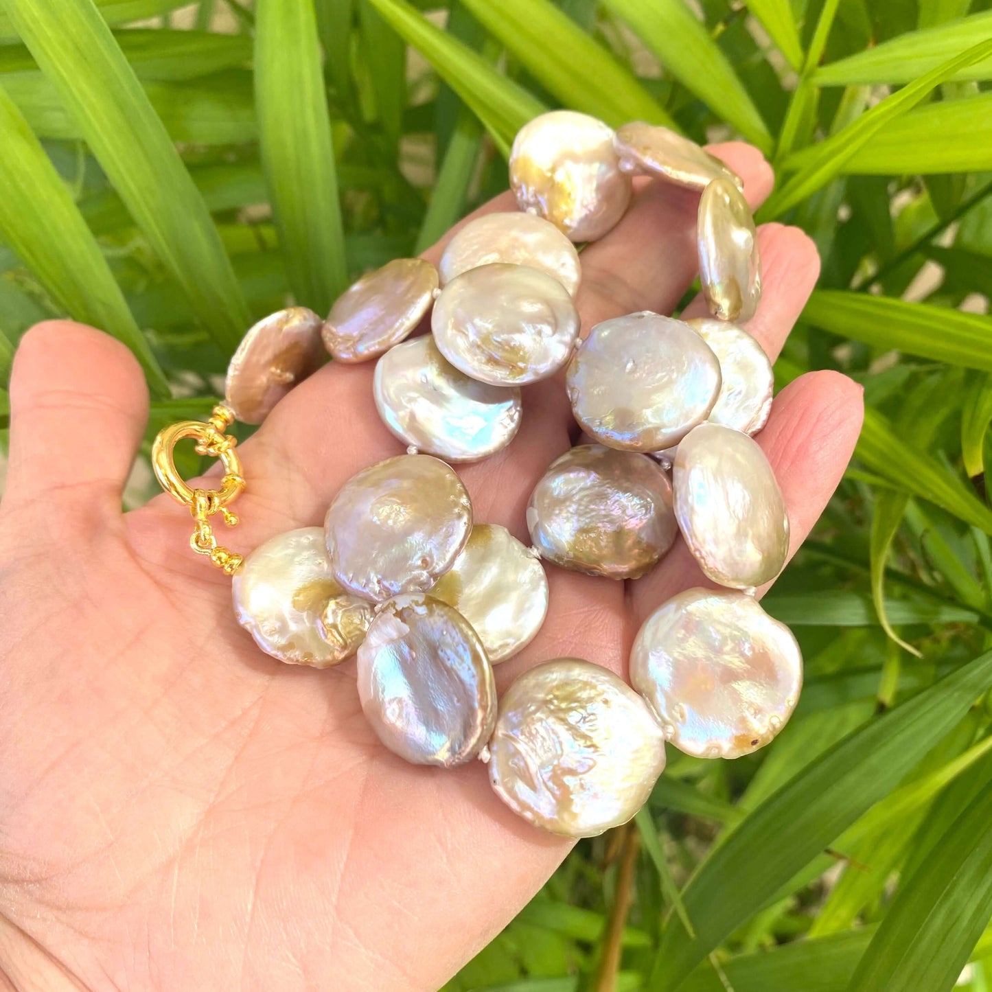 Large coin pearl necklace held in hand against green leaf background