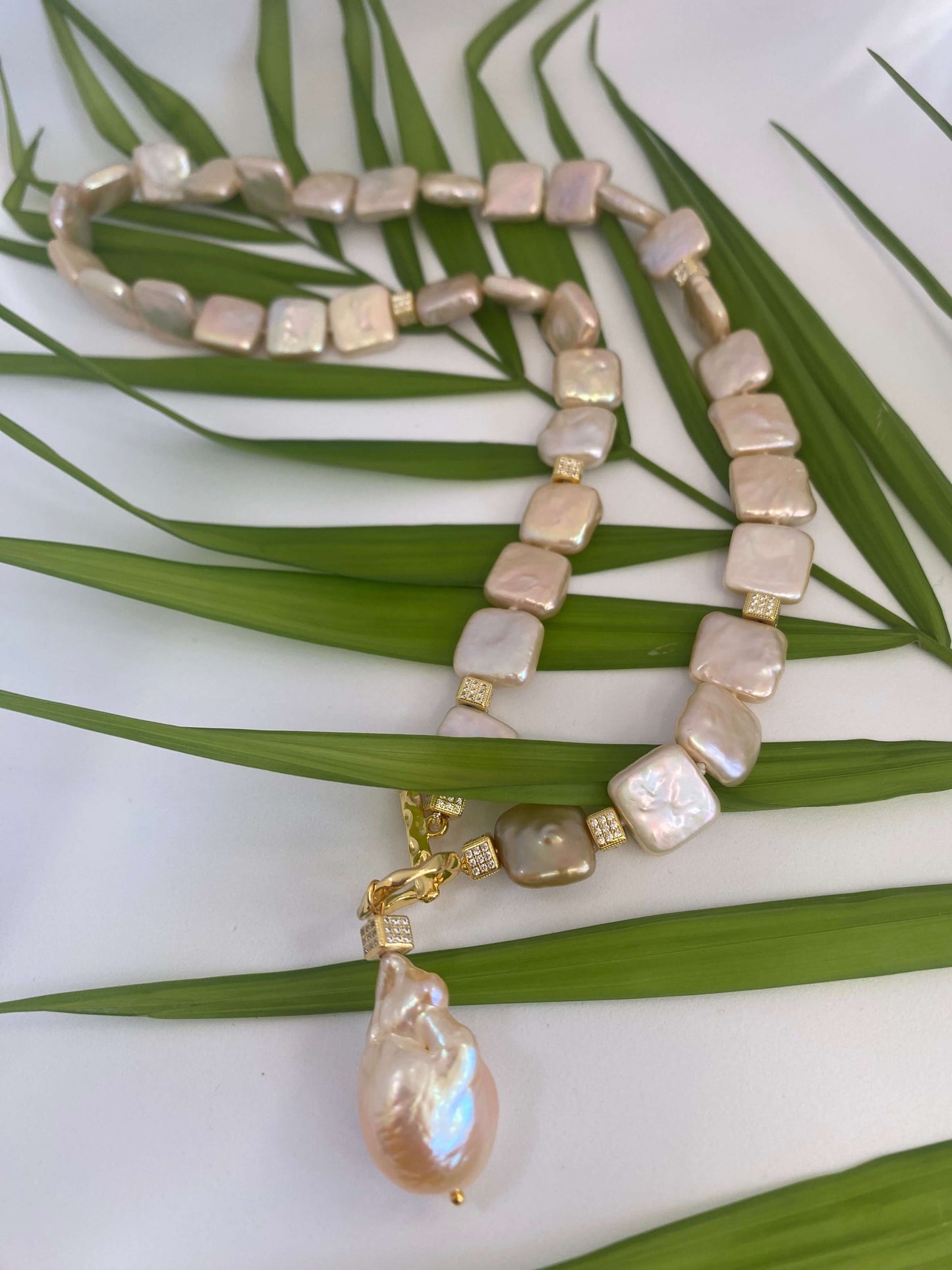 Golden baroque pearl toggle necklace displayed on green leaf branch — elegant handcrafted pearl jewelry photographed in natural light