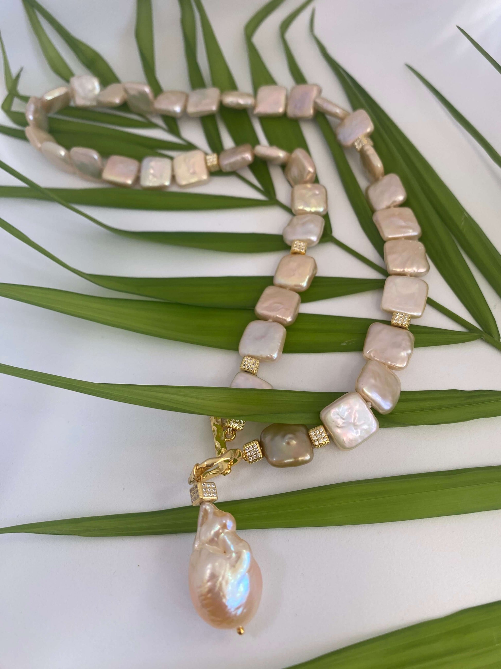 Golden baroque pearl toggle necklace displayed on green leaf branch — elegant handcrafted pearl jewelry photographed in natural light