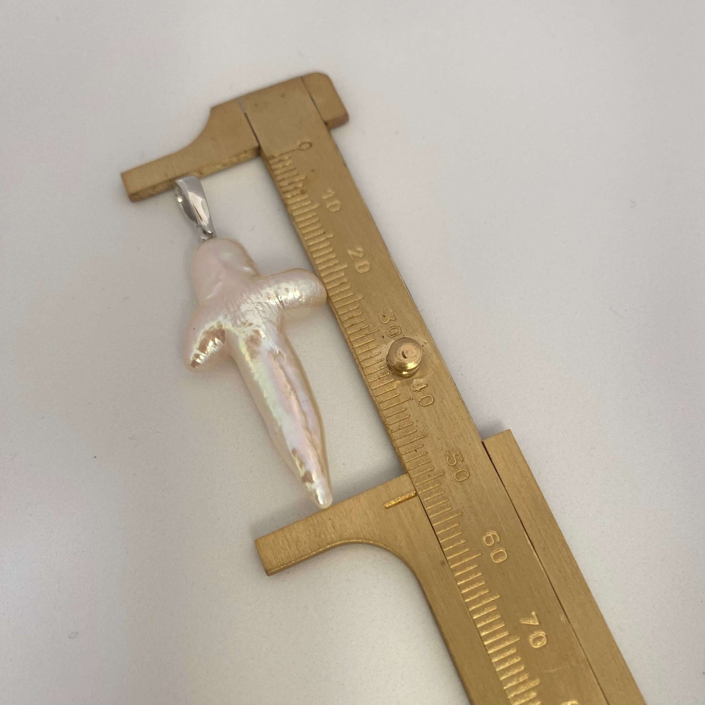 Baroque pearl cross pendant close-up beside ruler showing size and natural luster.