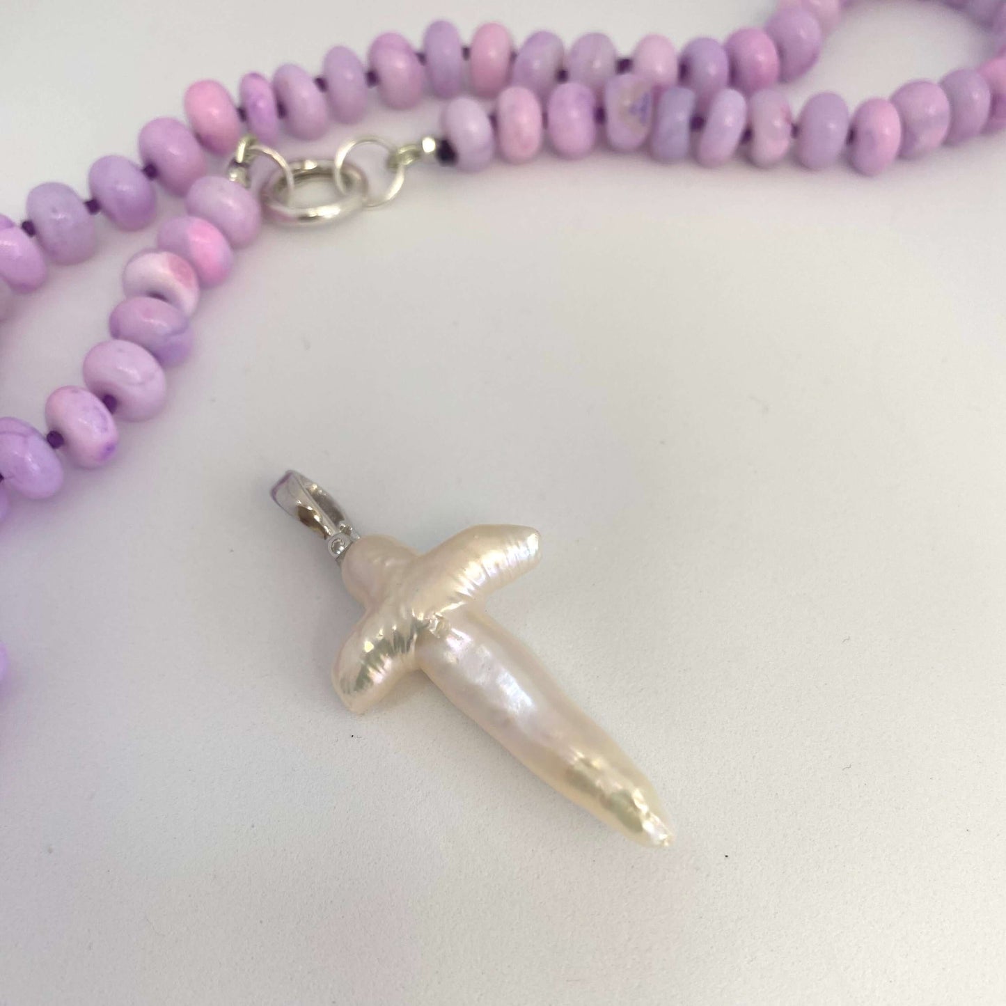 → Baroque pearl cross pendant close-up beside lavender opal necklace, luminous handcrafted detail.