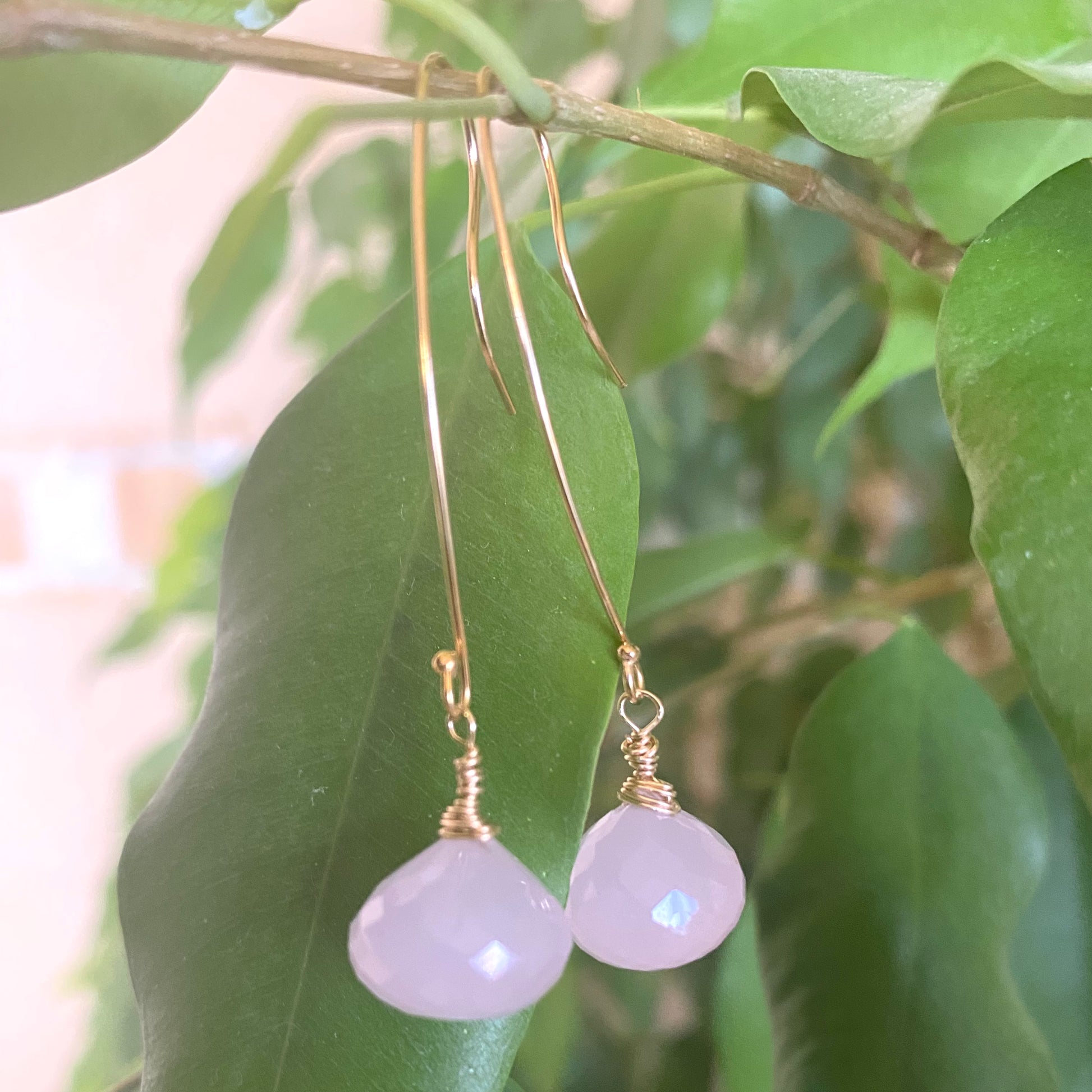 Rose quartz threader earrings with briolettes hanging against green leaves.