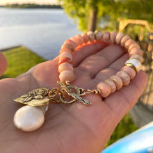 Load image into Gallery viewer, Pink opal bracelet with heart and baroque pearl charm displayed on a hand by the water.
