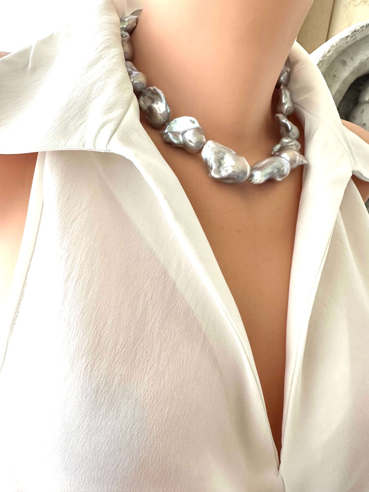 Baroque pearl necklace with silver details, showcasing large silver-grey baroque pearls on a stylish blouse.