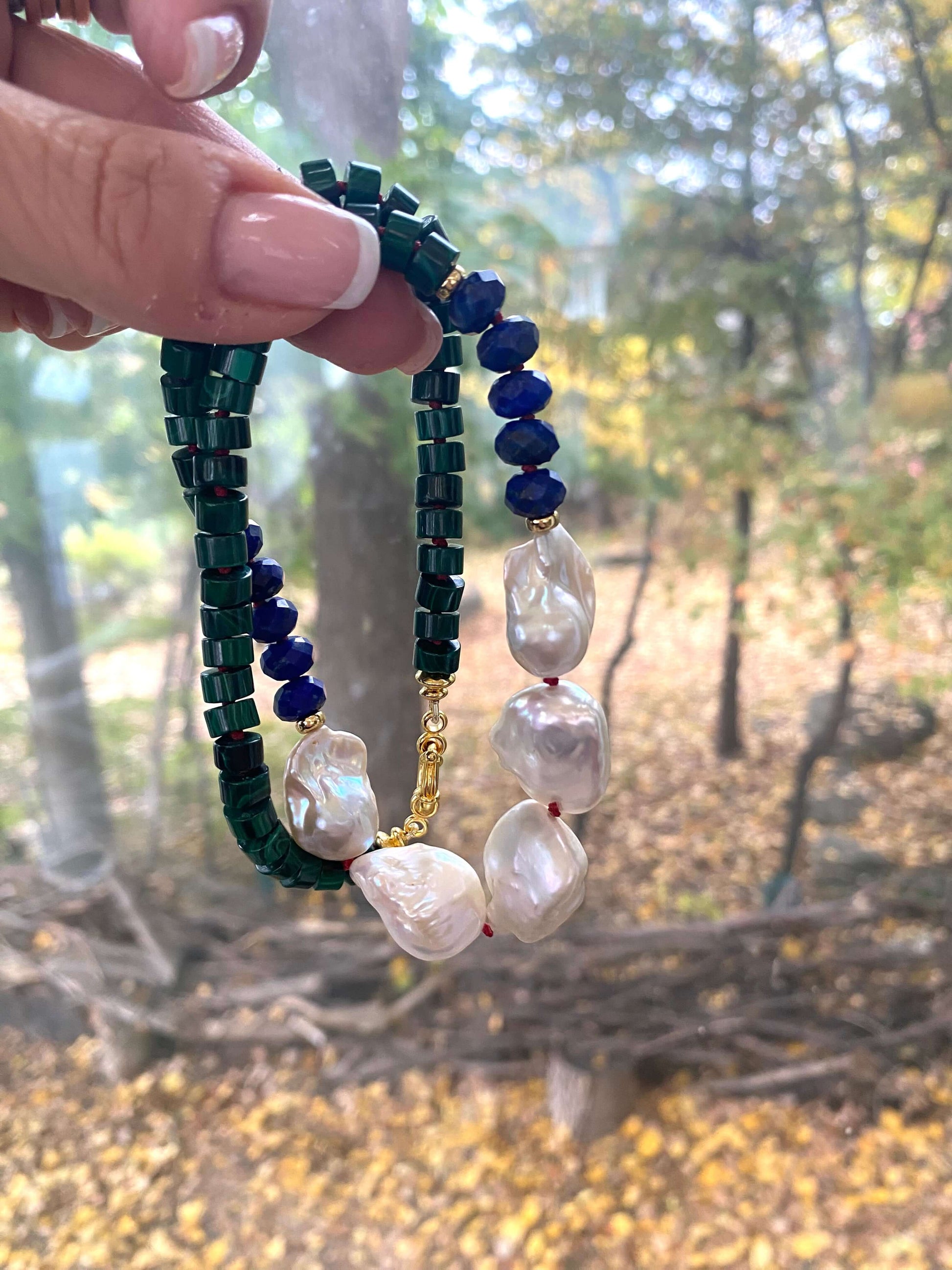 Malachite Lapis Lazuli Baroque Pearl Necklace held in hand against green leaf backdrop, designed and handmade in Canada.