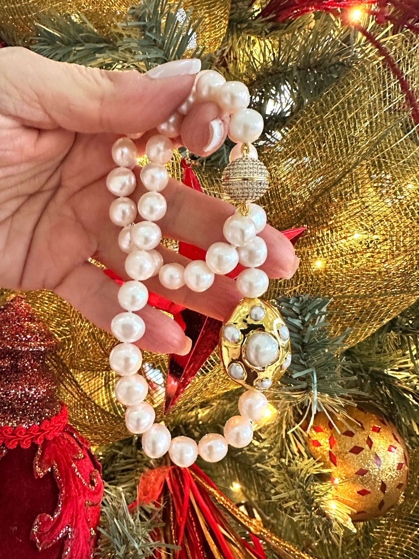 White potato pearl necklace with gold focal accent being held in hand, adorned with festive decorations.