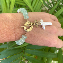 Load image into Gallery viewer, Chalcedony bracelet with cross pearl pendant and daisy charm on a hand against green foliage.
