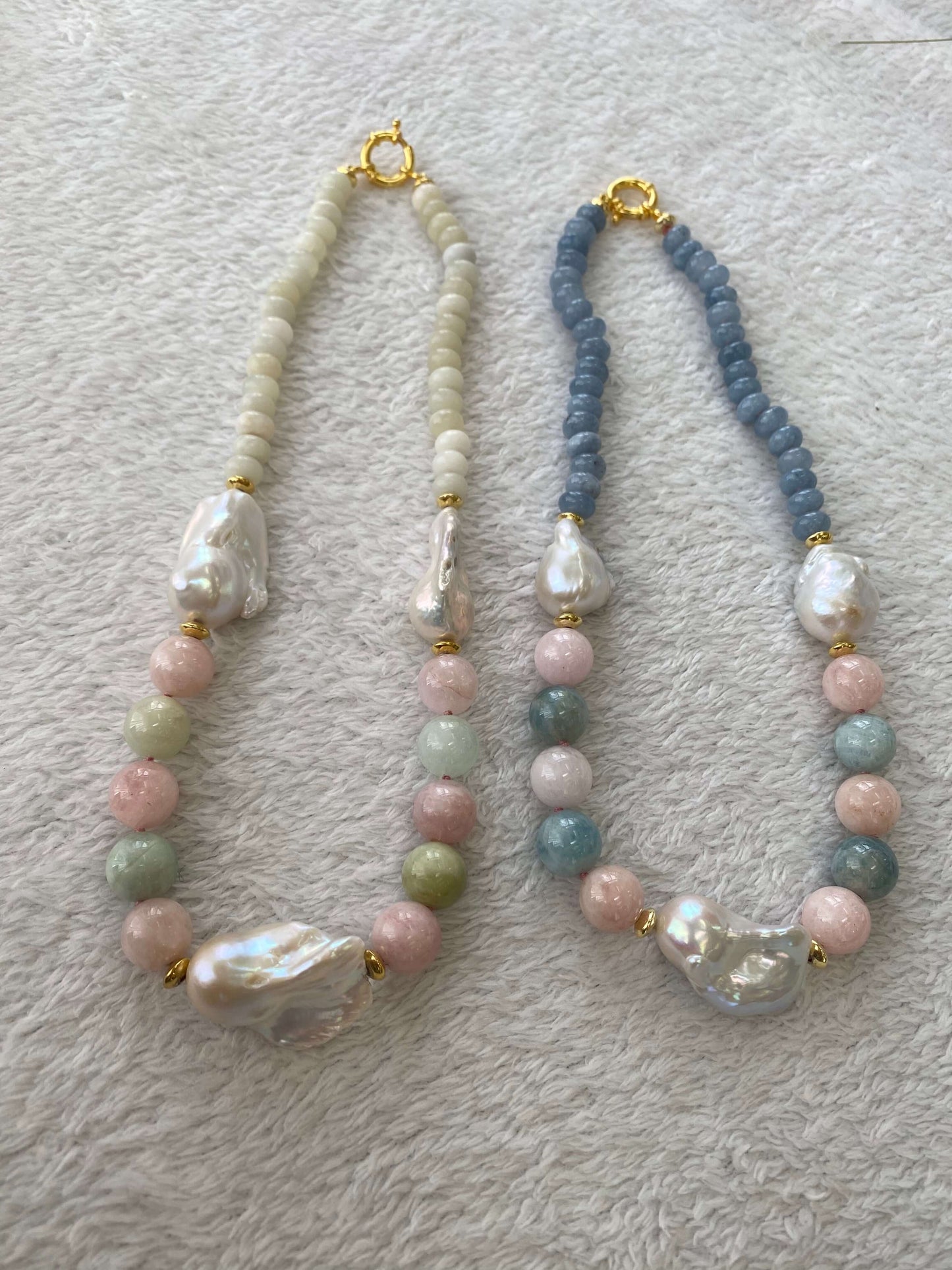 Morganite and jade necklace with baroque pearls beside blue gemstone necklace on white mat, showcasing color contrast and design variety.