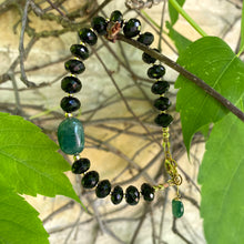 Load image into Gallery viewer, Spinel emerald bracelet featuring black spinel rondelle beads and vibrant green emerald accents among lush leaves.
