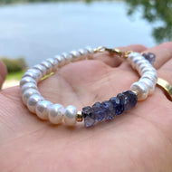 Iolite pearl bracelet featuring blue iolite rondelle beads and luminous white pearls held in a hand by a lake.