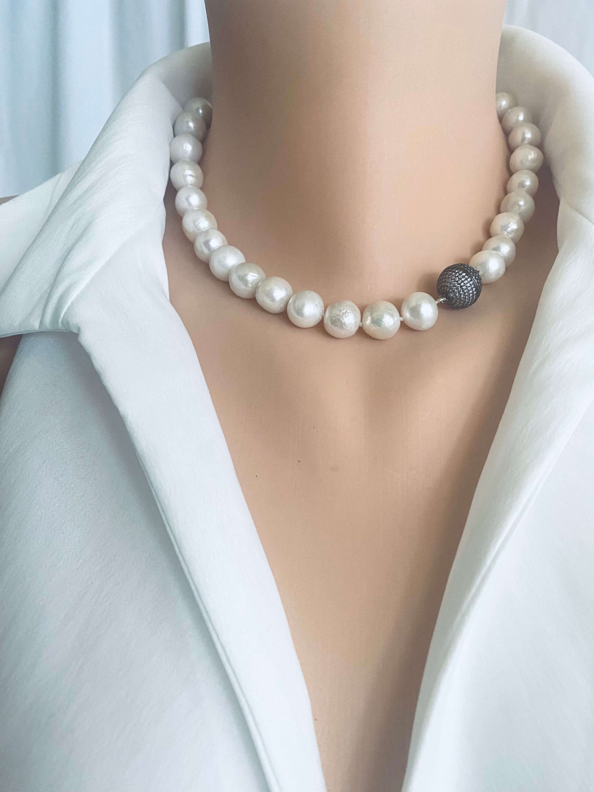 White Edison pearl necklace with gunmetal pavé magnetic clasp worn around the neck, featuring large luminous round pearls.
