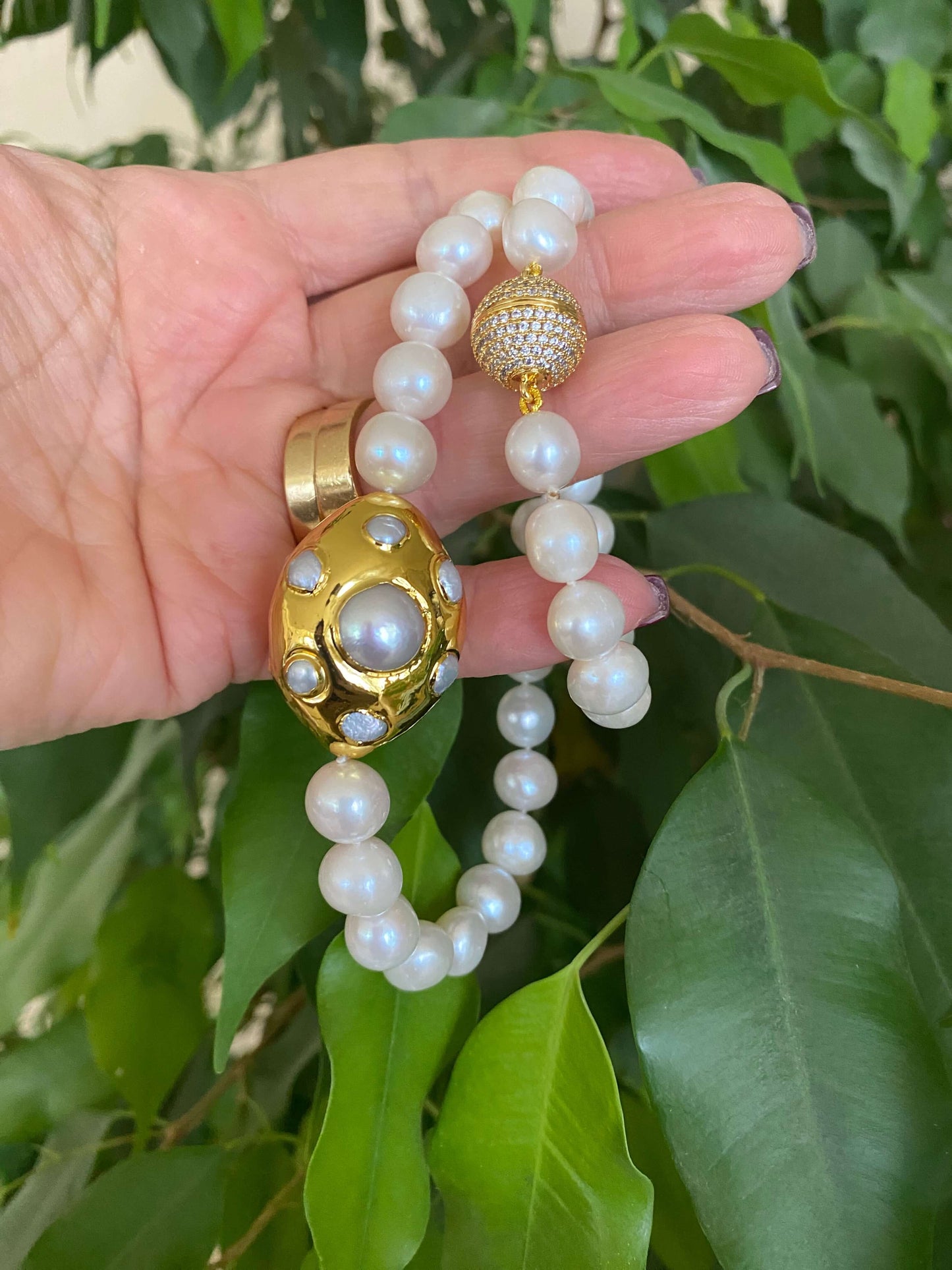 Hand holding a white potato pearl necklace with gold focal accent, showcasing the beautiful freshwater pearls.