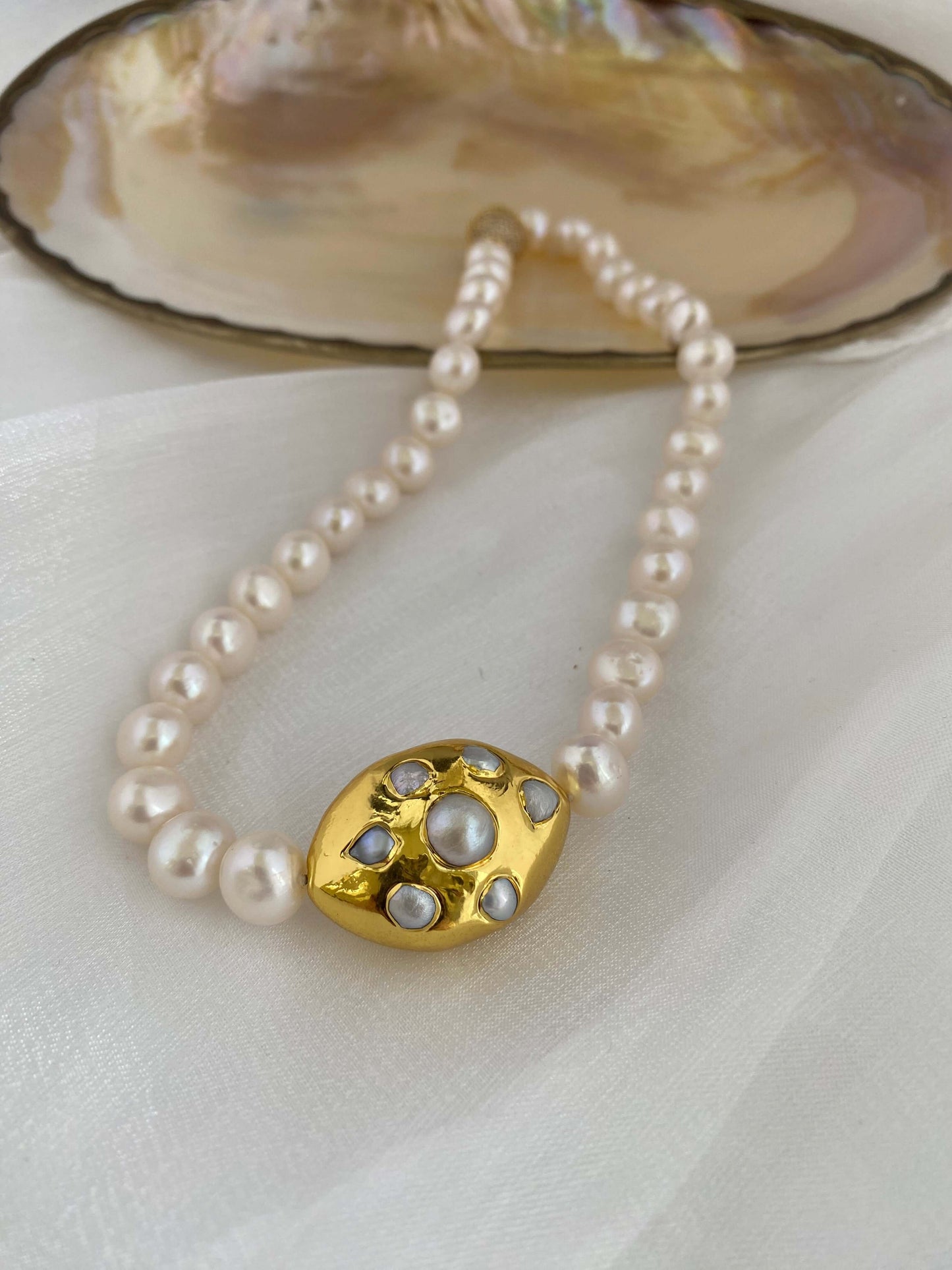 White potato pearl necklace with gold focal accent on a soft surface.