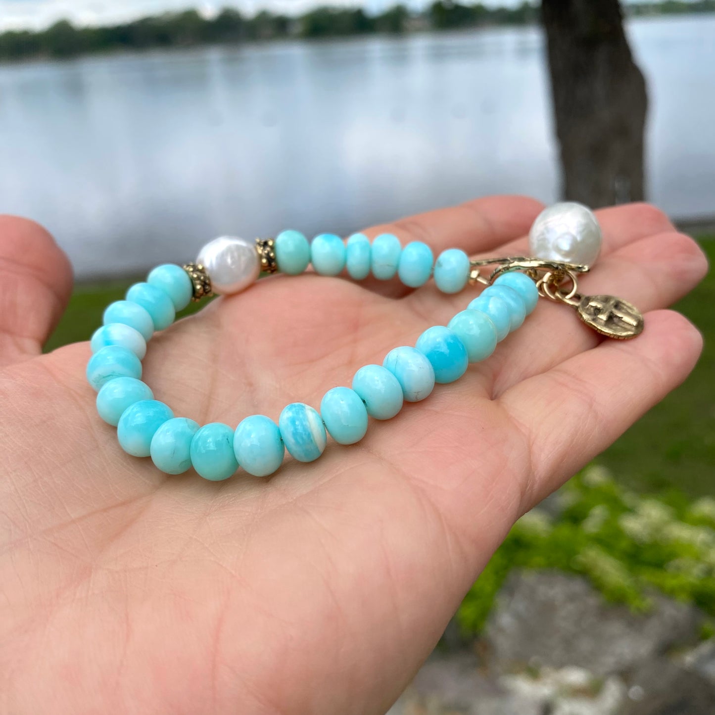Sky blue opal bracelet with baroque pearls and cross charm, showcasing serene colors and artisan craftsmanship.